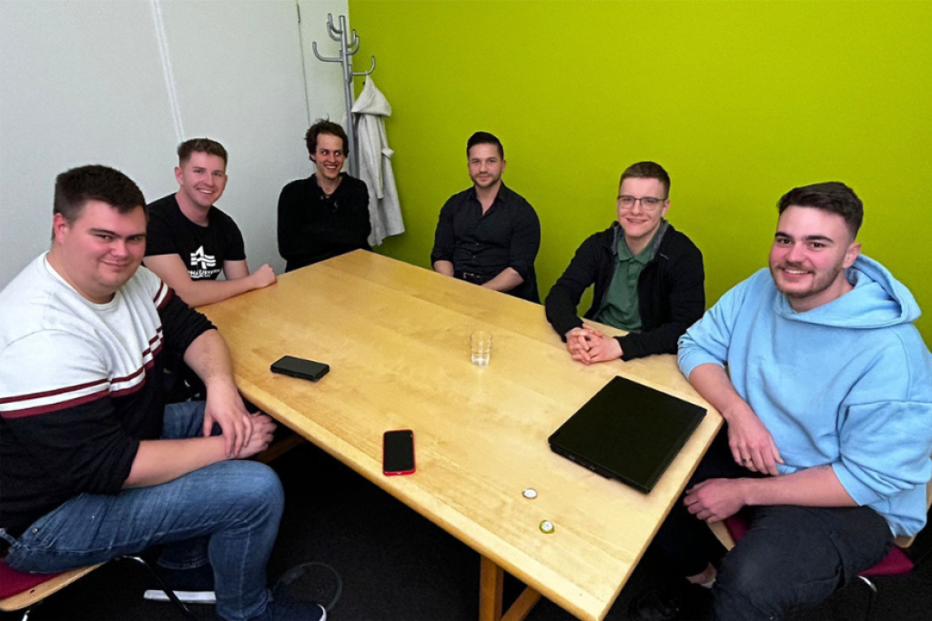 6 Jungs sitzen an einem Tisch und lächeln in die Kamera.